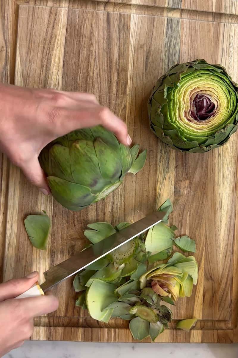 Rinse the artichoke with water and pat dry with a paper towel. Take the artichoke and remove any outer part leaves that may seem dry. Cut the stem off, and an inch from the top until the inside is exposed.