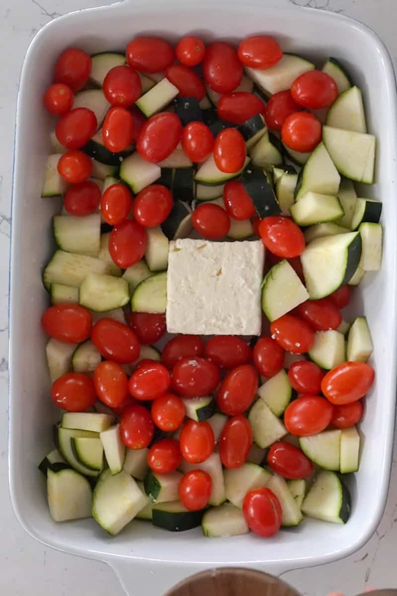 Preheat the oven to 400 °F. In a large baking dish, place the block of feta cheese in the middle and add the zucchini, cherry tomatoes and garlic around it.