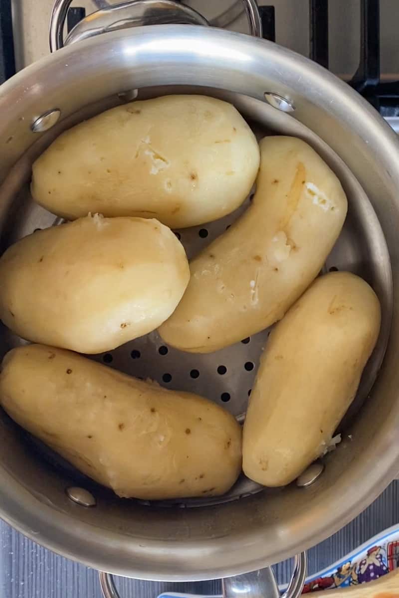 Start by taking the skin off the potatoes with a vegetable peeler and place them in a pot of boiling water or a steamer if you have one. Keeping boiling on high heat until potatoes are easily pierced with a paring knife, about 20 minutes.   Take the potatoes out but do not pour out the water.