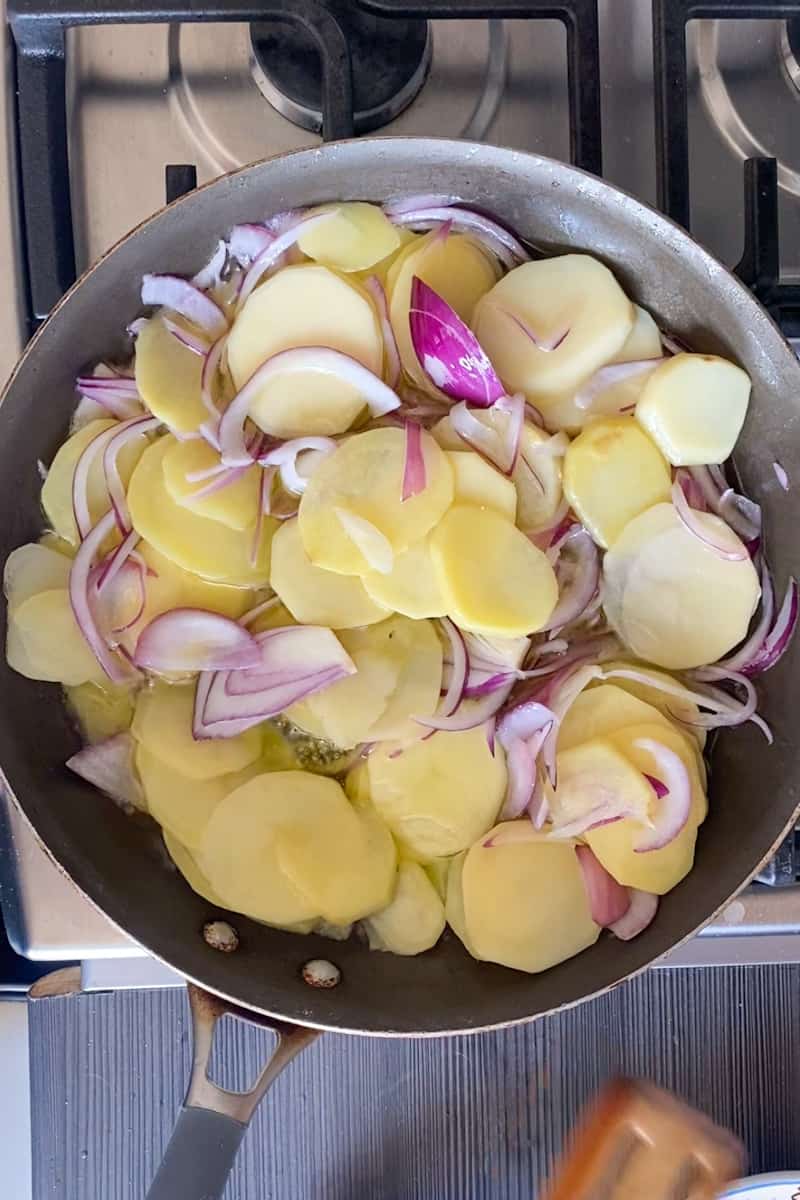 Using a medium skillet, heat up the olive oil on medium heat and wait for the oil to shimmer. Add the sliced onion, potatoes, and salt into the skillet. With a wooden spoon, toss the vegetables for about 6-9 minutes. Reduce heat until the oil is bubbling at a slow pace. Toss potatoes gently every few minutes, until they are tender when pierced with a small knife.  Do not let the potatoes break or brown, reduce the heat if necessary.