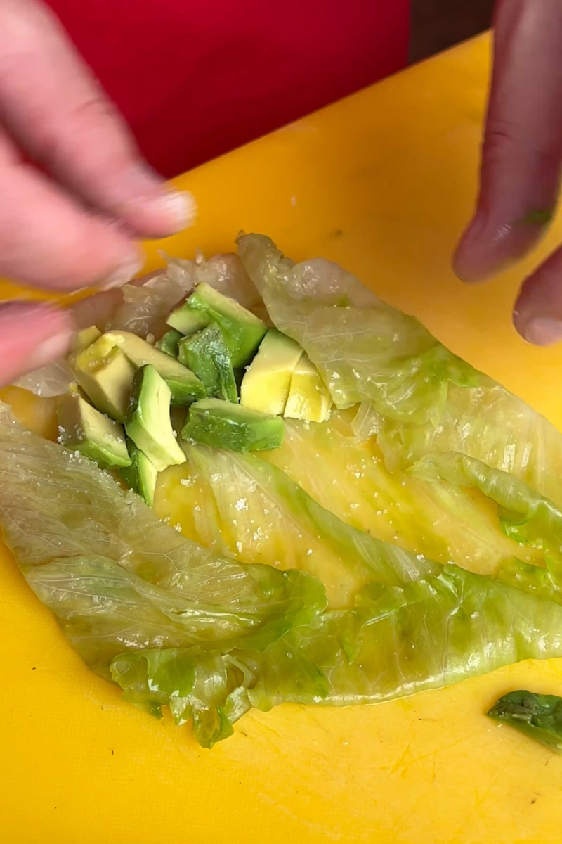Lay a leaf flat on a surface and add the diced avocado on it. Season with salt. Roll the lettuce into the shape of an egg roll. Repeat with the rest. 