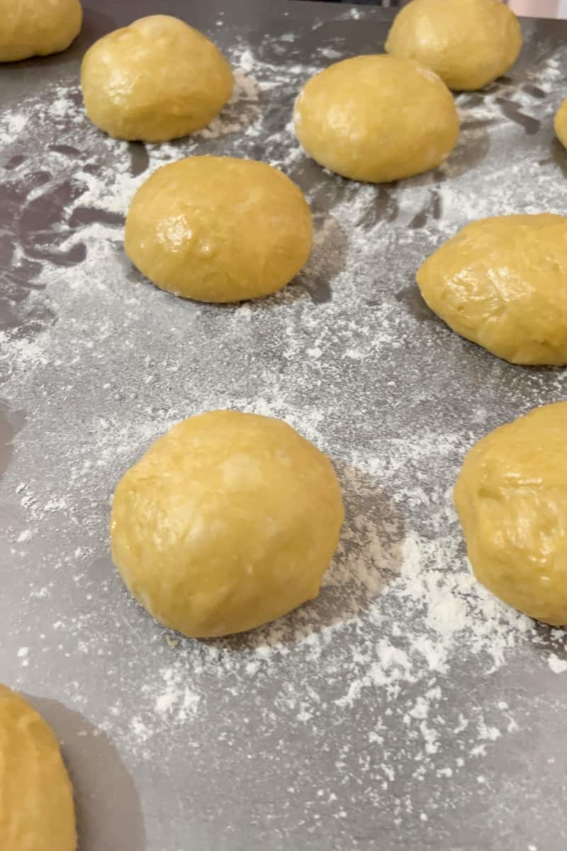 Once the dough is doubled in size, place this on a floured surface. Divide the dough into 16 small balls. To shape the balls, flour your hands and press the ball down while making rotating motions to form each ball. Place each ball on a greased baking sheet and continue with the rest. Make sure they are not too close to each other. You may need multiple baking sheets.