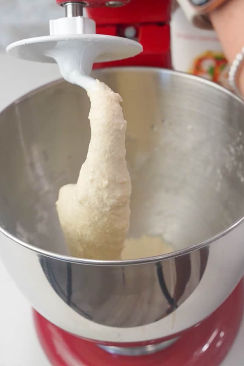 In a mixing bowl, combine the flour, yeast, sugar, and salt. Mix these dry ingredients together. Gradually add the lukewarm water to the dry ingredients while stirring. Continue to mix until a dough forms. Knead the dough on a floured surface for about 5-7 minutes until it becomes smooth and elastic. Alternatively, you can use a mixer with a dough hook attachment. Place the dough in a lightly greased bowl, cover it with a kitchen towel, and let it rise for about 12 hours or until it doubles in size.