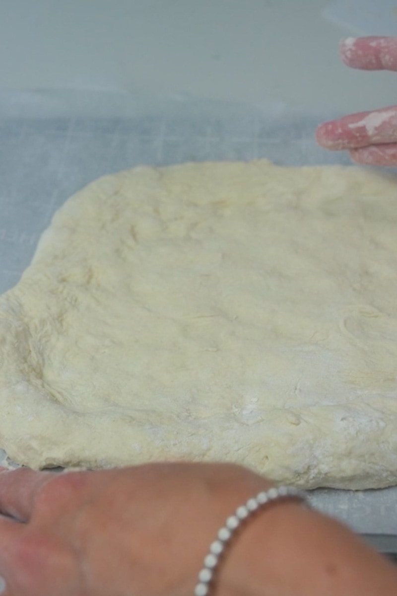 Preheat oven to 500°F. Punch down the risen dough to release any air bubbles. Divide it into two equal portions if you want to make two smaller pizzas or keep it whole for a larger one. On a floured surface, roll out the dough into your desired pizza shape. You can make it round, square, or any shape you prefer.