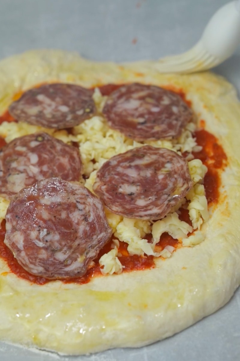 Carefully remove the preheated pizza stone or baking sheet from the oven. Place the rolled-out dough on a piece of parchment paper (for easy transfer) and then onto the hot pizza stone or baking sheet. Spread a thin layer of marinara sauce over the dough, leaving a small border around the edges for the crust. Sprinkle a generous amount of shredded mozzarella cheese over the sauce. Add your choice of pepperoni or salami slices on top of the cheese.