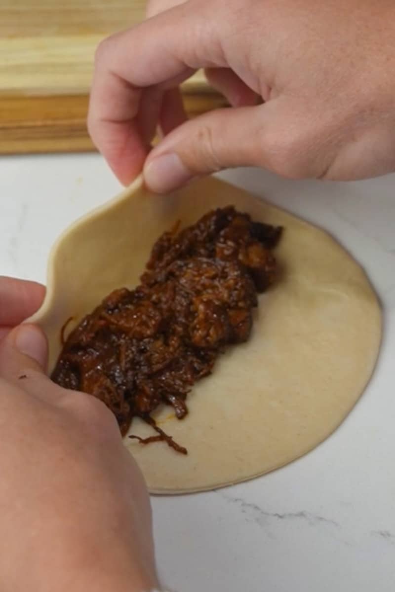 Cook the Pork: In a large, heavy-bottomed pot, heat some oil over medium-high heat. Add the pork cubes and brown them on all sides. Pour in the chili sauce you made and stir to coat the pork evenly. Add the bay leaf and 4 cups of beef broth. Stir well. Reduce the heat to low, cover the pot, and let the birria simmer for 2-3 hours or until the pork is tender and the flavors meld together. You may need to add more beef broth if the mixture becomes too thick during cooking. Adjust salt and pepper to taste. Assemble the Empanadas: Preheat your oven to the recommended temperature for the empanada discs. Place a spoonful of the birria filling onto each empanada disc. Fold the discs over to create a half-moon shape and seal the edges by pressing with a fork.