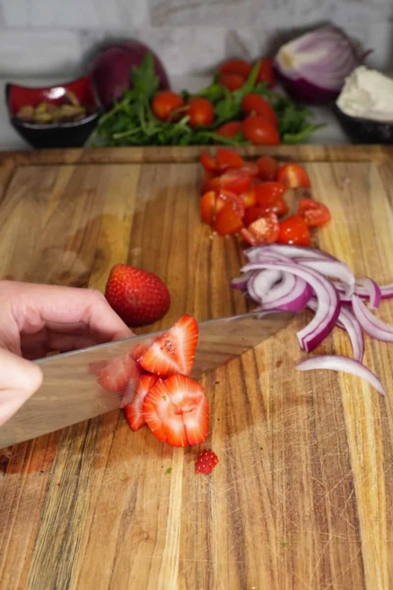 In a large salad bowl, combine the arugula, cherry tomatoes, red onion, and dried cranberries (or strawberries if using).